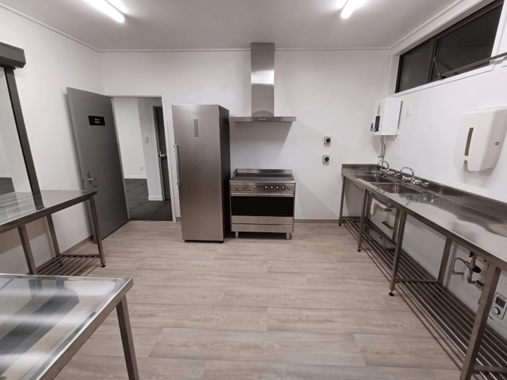 Compact stainless steel kitchen with range, extraction hood, sink bench, and timber floor