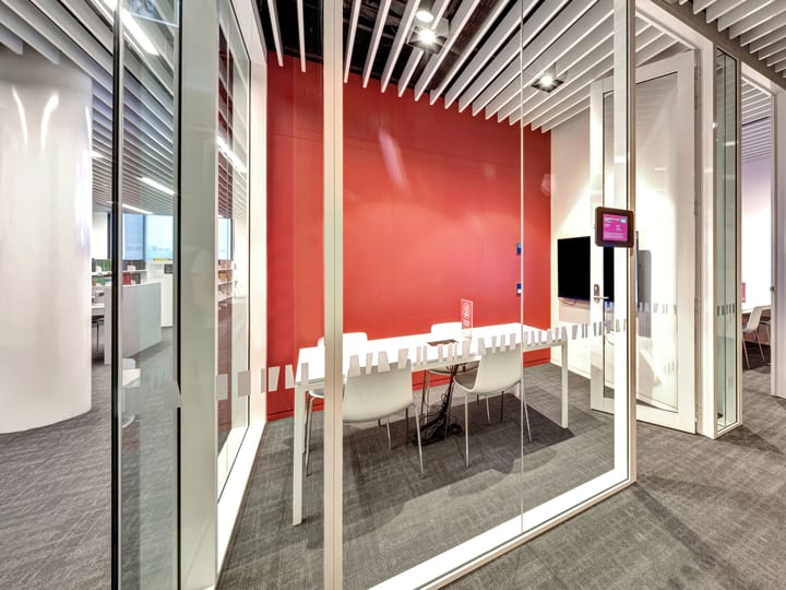 Glass-walled meeting room with red feature wall, table and white chairs