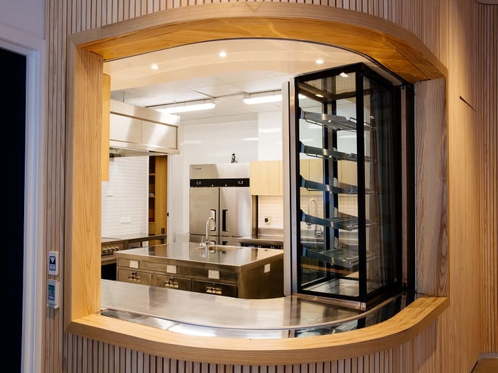 Kitchen servery viewed through an arched timber-framed pass-through window