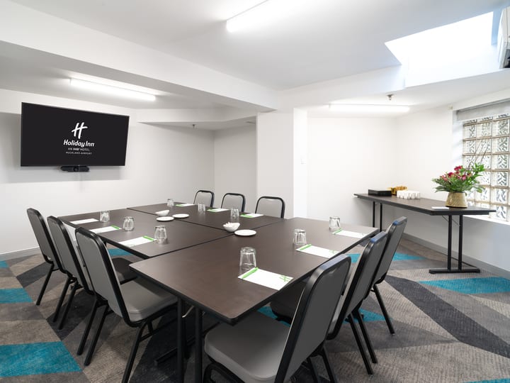 Small meeting room with a square table arrangement, wall-mounted screen, and patterned carpet