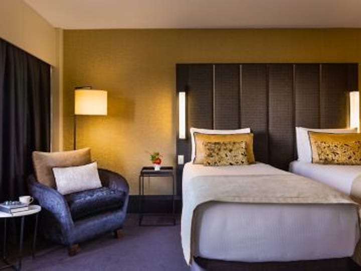 Twin-bed hotel room with upholstered headboard and armchair