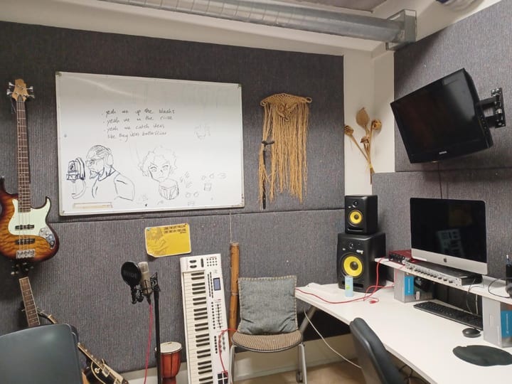 Recording studio room with guitars, keyboard, speakers, computer setup, and whiteboard