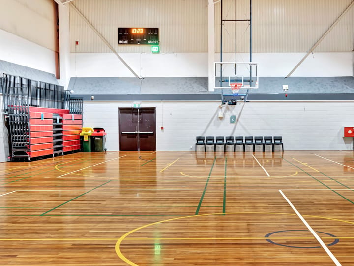 Timber-floored sports hall with basketball hoop, scoreboard and retractable bleacher seating