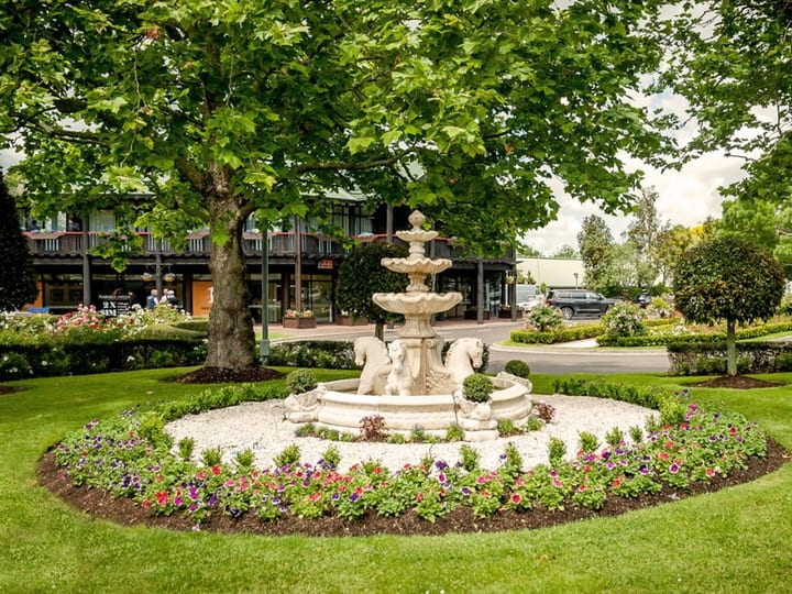 Ornate stone tiered fountain surrounded by a circular flower bed and mature trees