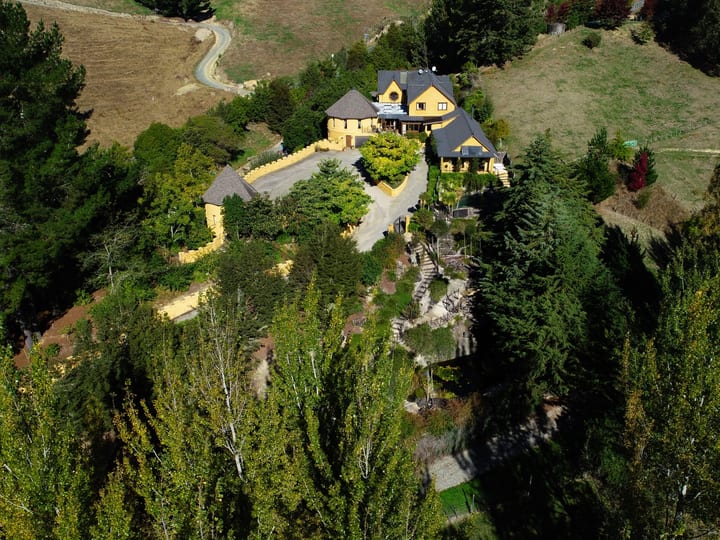 Aerial view of yellow stone castle-style building set into wooded hillside