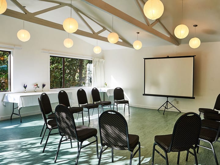 Light-filled room with vaulted ceiling, globe pendants, chairs in rows and projection screen