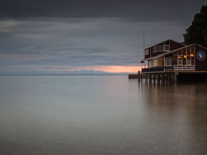 Timber clubhouse building on piles over water at dusk