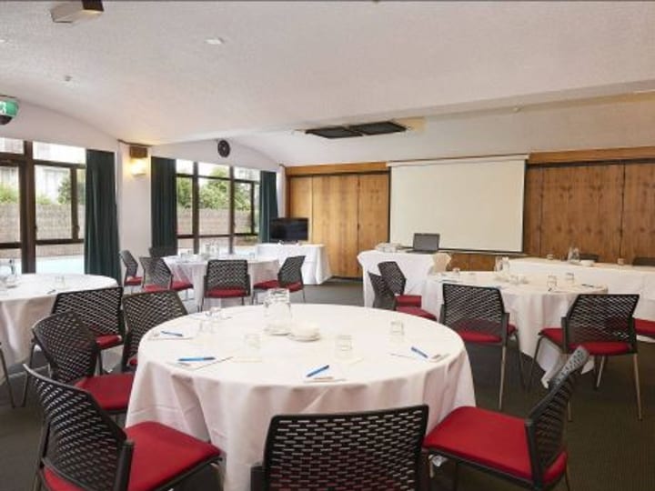Function room with round tables, timber wall panels and projection screen