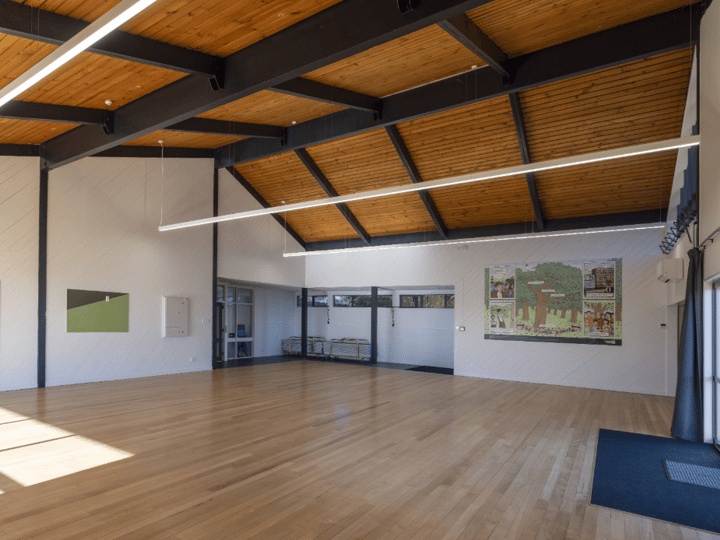 Large hall with exposed steel roof trusses, multicoloured carpet and artwork