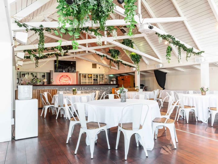 Open function space with exposed white trusses, hanging greenery and round tables set for event