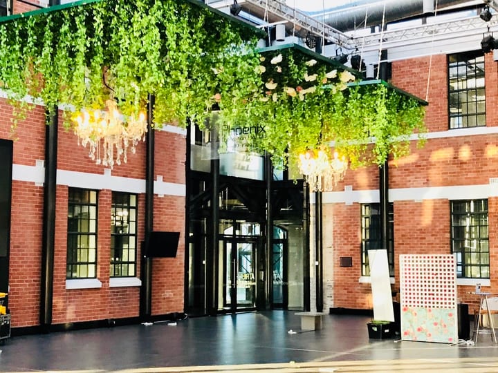 Industrial brick atrium interior with hanging greenery, chandeliers, and dark polished floor