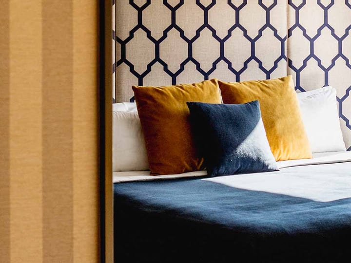 Hotel bed with patterned headboard and ochre cushions