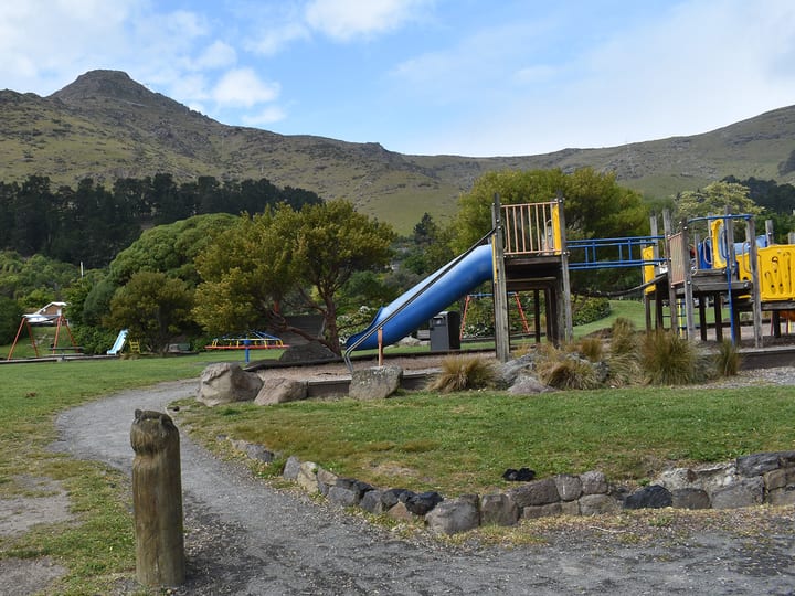 Park with playground equipment, trees, and hill backdrop
