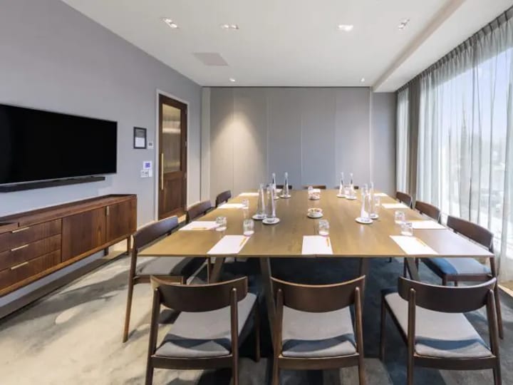 Hotel meeting room with square table layout, leather chairs, and wall-mounted TV