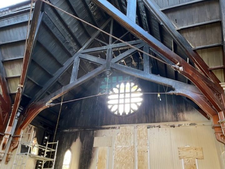 Church interior under repair with exposed timber arch trusses and rose window