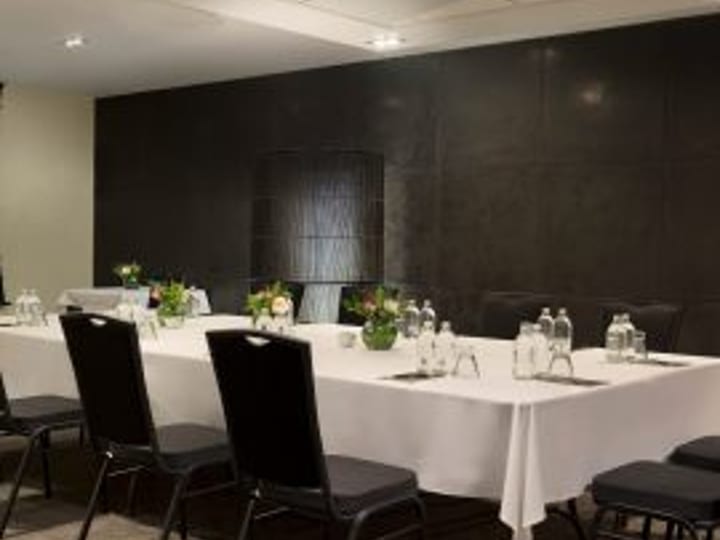 Small meeting room with U-shaped white-clothed table, black chairs, and dark feature wall