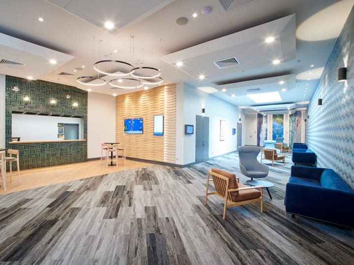 Contemporary hotel lobby with circular pendant lighting, tiled feature wall, striped carpet, and lounge seating