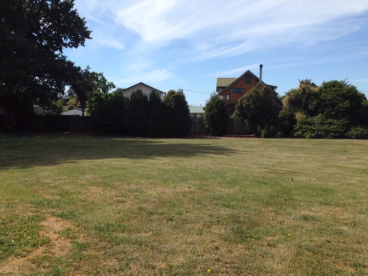 Open lawn area with trees at boundary and residential buildings beyond