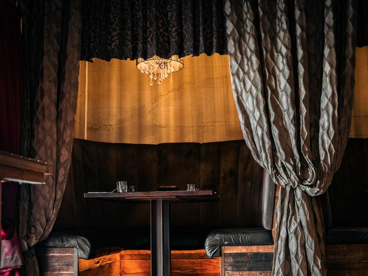 Dark draped fabric booth with leather bench seating, small table, and small chandelier overhead