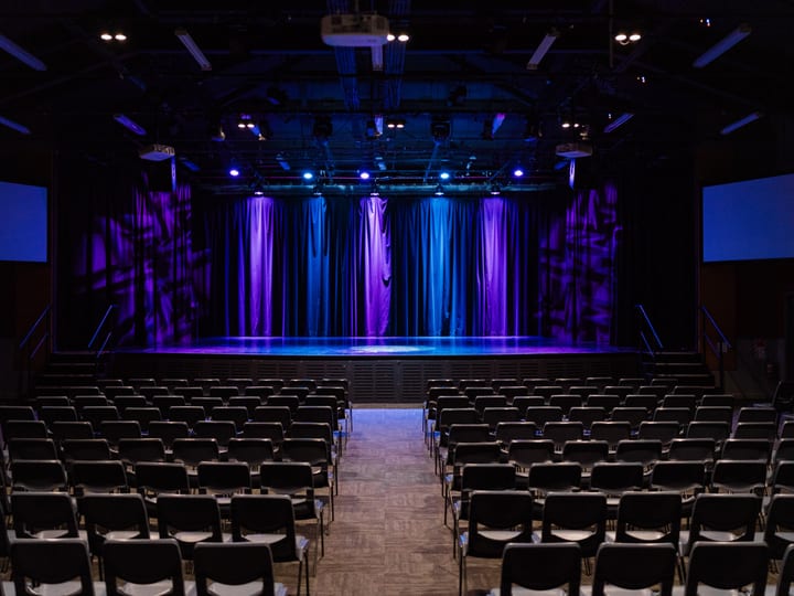Large performing arts auditorium with stage, curtains lit in purple and blue, and rows of seats