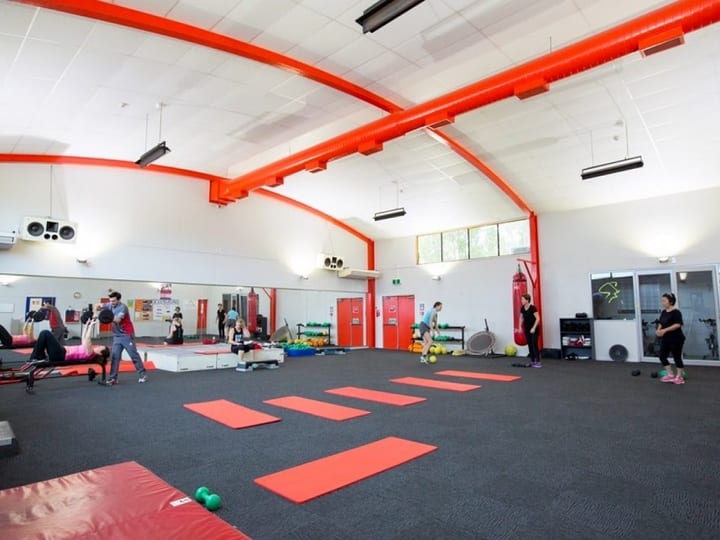 Fitness studio with red structural beams, mirrored wall and exercise mats on dark floor