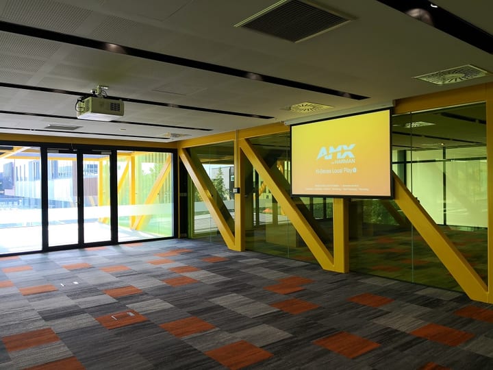 Open event hall with yellow steel frames, projection screen and colourful carpet