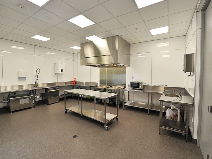 Commercial kitchen with stainless benches, large extraction hood, wall-mounted appliances, and oven range