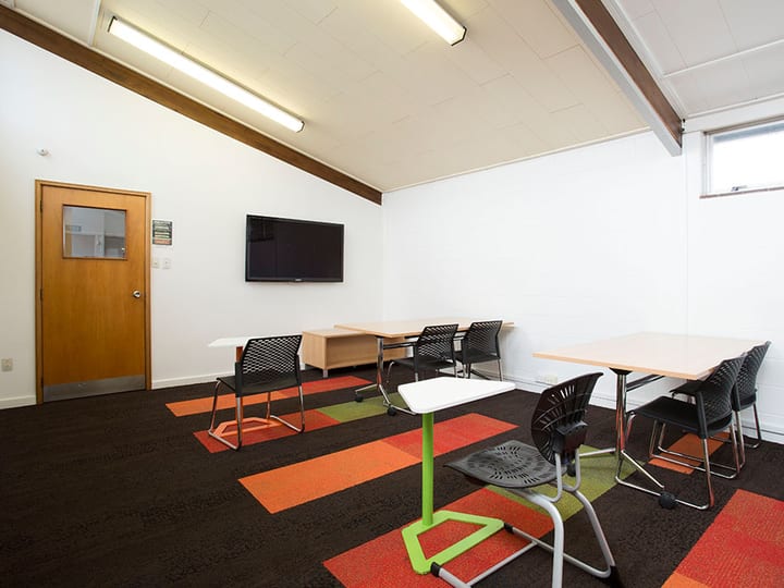Small meeting room with tables, chairs and wall-mounted screen