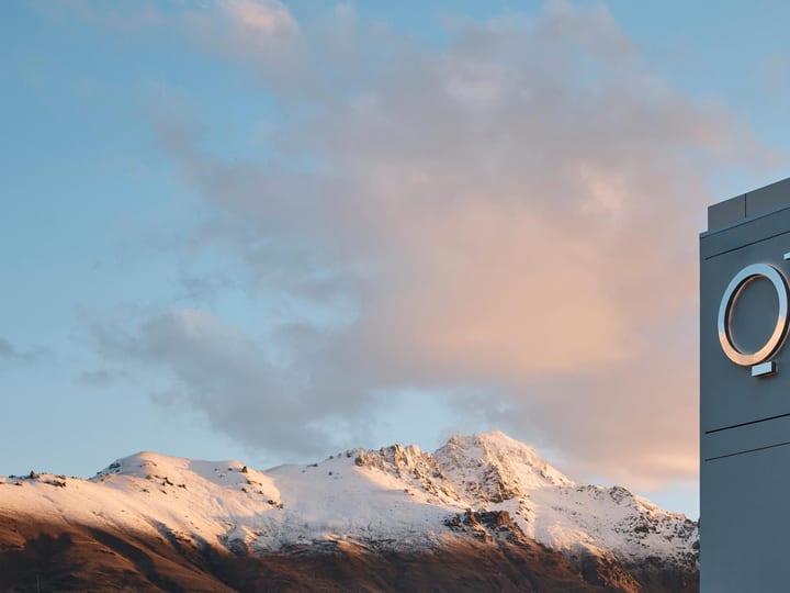 Grey rendered building exterior with brand signage, snow-capped mountains behind