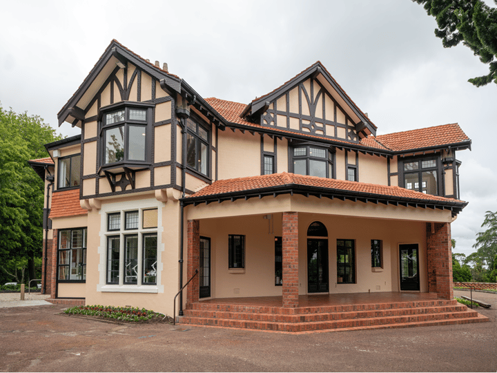 Two-storey cream and red-brick Tudor-revival homestead with terracotta tile roof, covered entrance porch