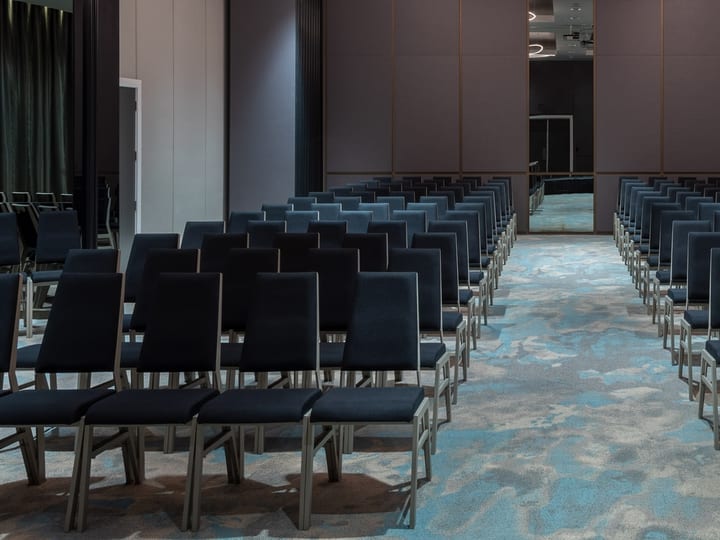 Hotel ballroom in theatre layout with rows of dark chairs and decorative lighting
