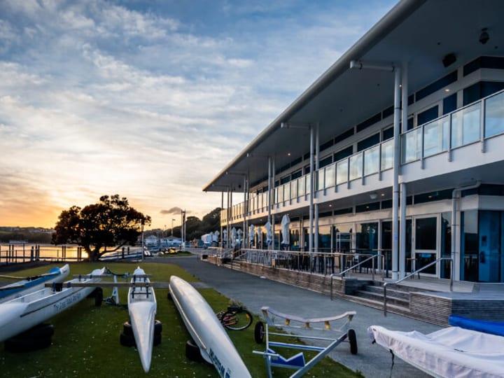 Two-storey waterfront function centre at sunset with boats on the foreshore
