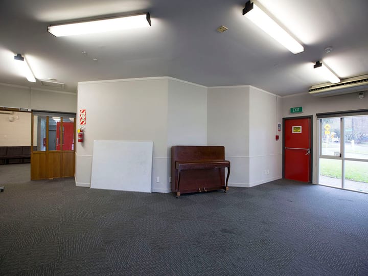 Open carpeted hall with whiteboard, upright piano, and red exit door