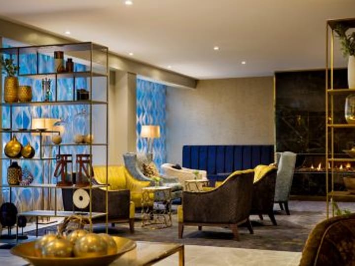 Hotel lounge with yellow and brown armchairs, open shelving with decorative objects, blue patterned wall panels