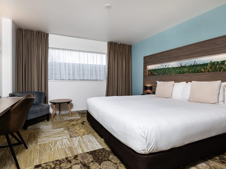 Hotel room with double bed, timber headboard, patterned carpet, and curtained window