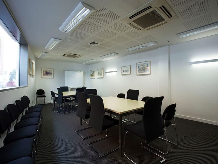 Meeting room with two sets of tables and black chairs, framed artwork on walls