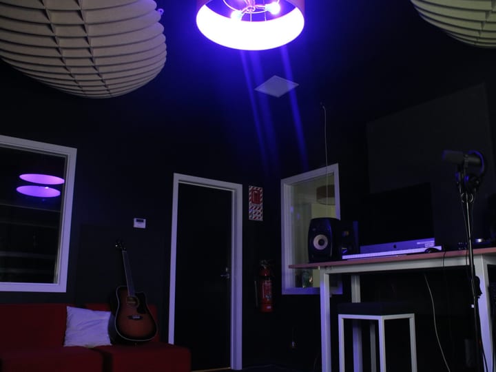 Dark room with blue UV pendant lights, red couch, guitar and audio equipment