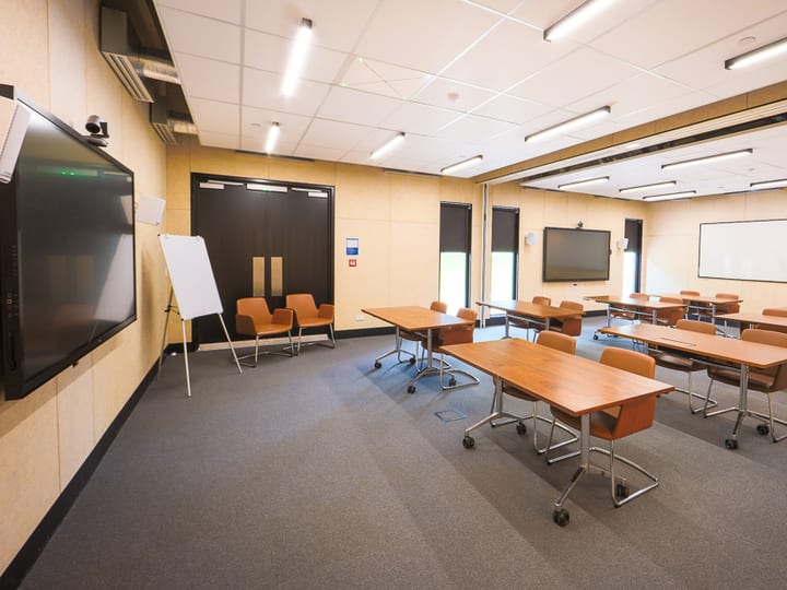 Classroom-style seminar room with rows of tables and orange chairs, and a large screen at the front