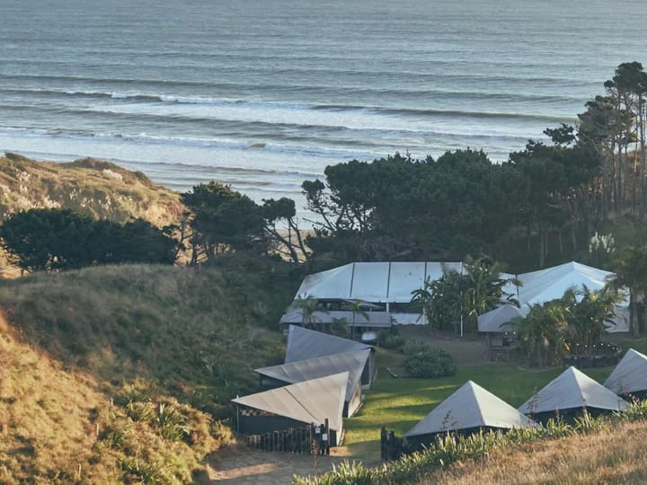 Aerial view of coastal retreat with tent structures on hillside above beach