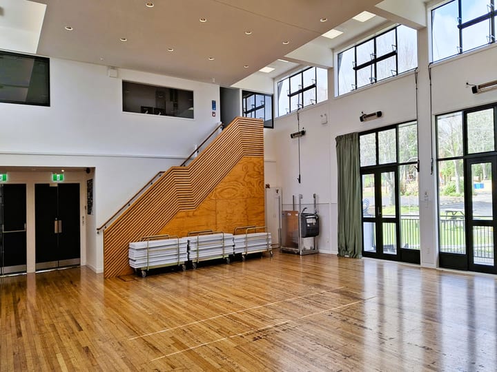 Hall interior showing timber stair feature wall, floor-to-ceiling windows and stacked trestle tables