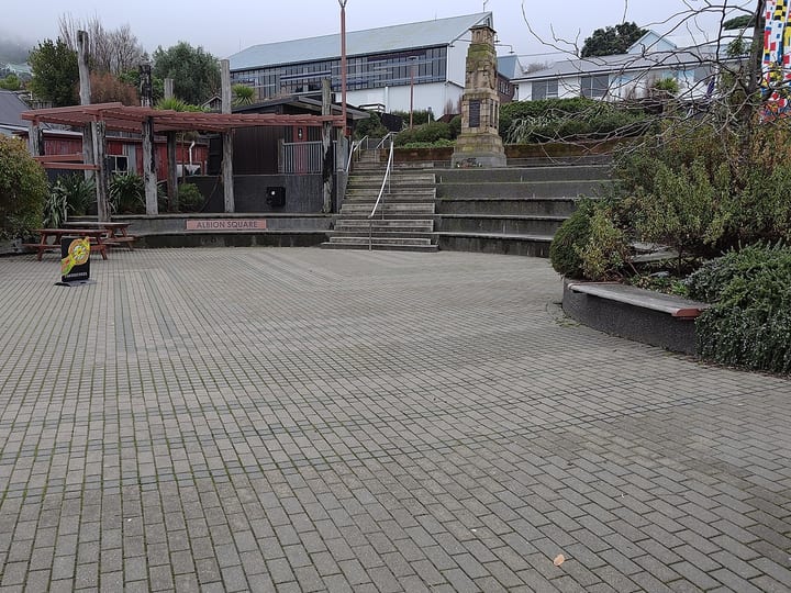 Open paved town square with seating, pergola structures, and memorial column