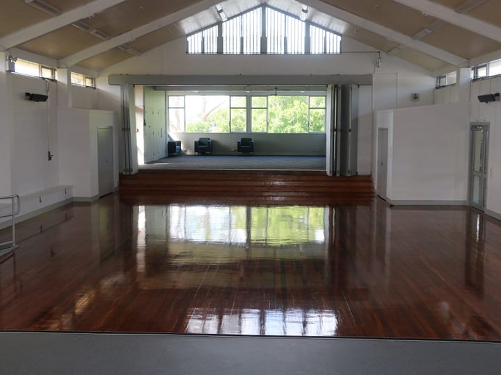 Hall interior with vaulted ceiling, polished timber floor, and raised platform seen from the stage end