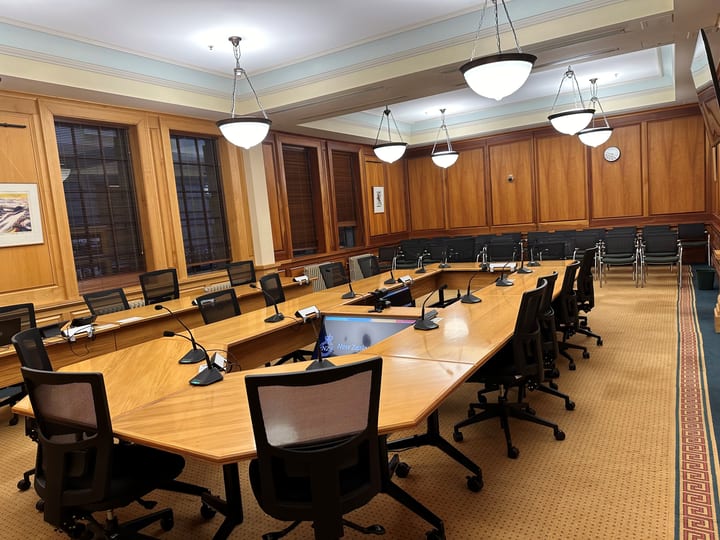 Formal meeting room with timber-panelled walls, large oval table, microphones and pendant lights