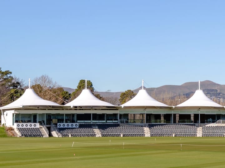 Cricket oval grandstand with distinctive peaked white canopy roofs and hills behind