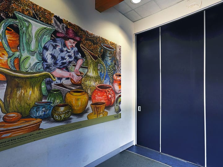 Wall mural of potter at wheel next to blue partition wall