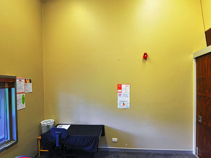 Plain room with yellow walls, single chair and small table, notices on wall