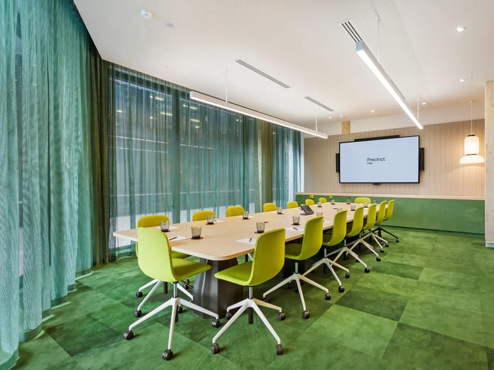 Meeting room with long timber table, green chairs, green carpet and large wall-mounted screen