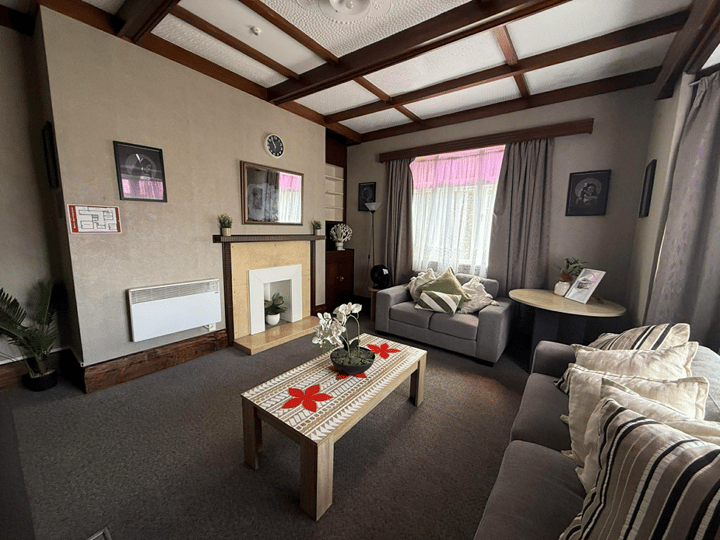 Carpeted lounge with exposed timber ceiling beams, fireplace, and sofas