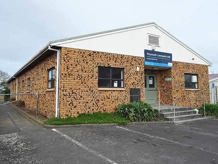 Tan brick hall from side angle showing double green doors and car park
