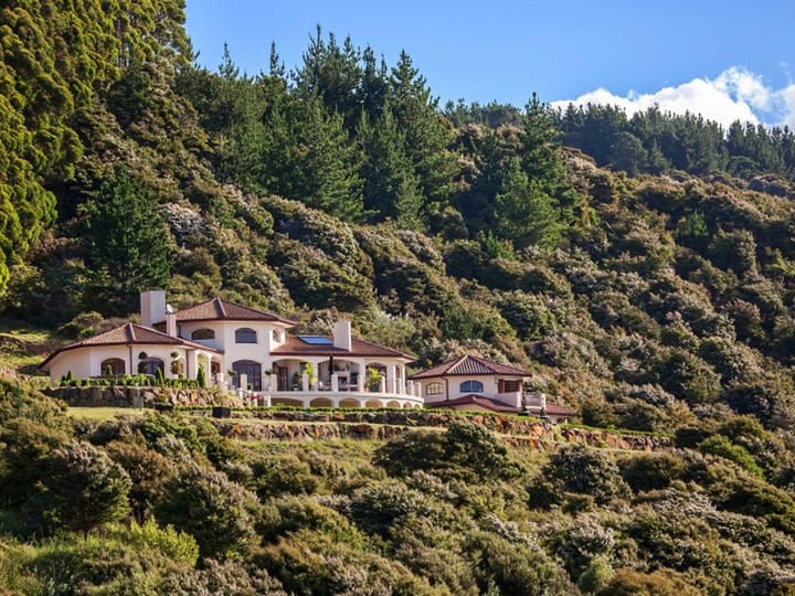 The full Mediterranean-style building seen from the hillside in daylight, set into forested slopes